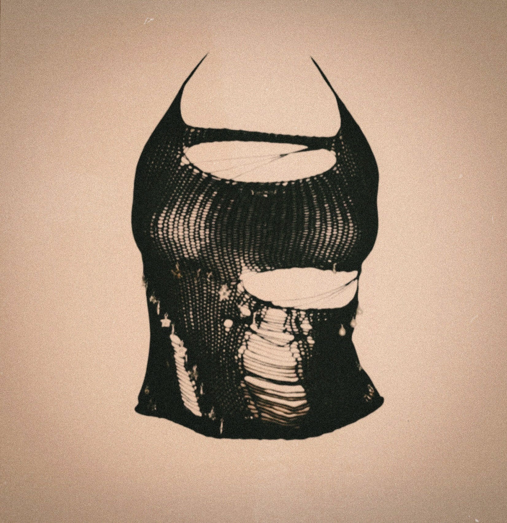 Black handcrafted deconstructed halter top with shredded mesh, sculptural cutouts and raw distressed detailing, photographed against a neutral textured backdrop.
